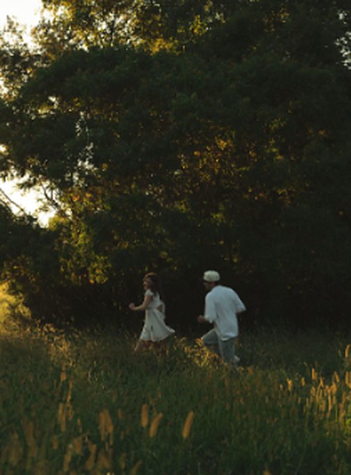 A couple running toward a tree line at sunset